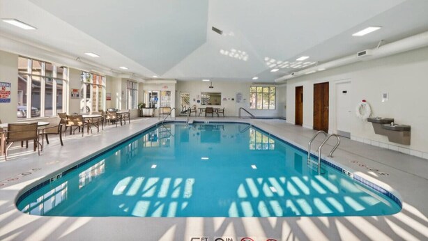 An indoor swimming pool with clear water, surrounded by tables and chairs, and a ceiling with recessed lighting. - Bushwood at Delton Grand (Wisconsin Dells)