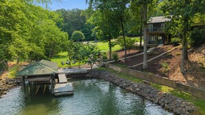 Une propriété au bord du lac, dotée d’un quai, d’un espace salon couvert et d’une maison avec un balcon donnant sur l’eau.