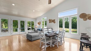 Un vaste espace de vie comprenant une table à manger, des chaises blanches, un canapé gris et un ventilateur de plafond.