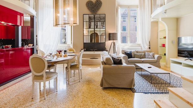 A modern living room with a dining area, a kitchen with red accents, a heart-shaped wall decoration, and a large window.