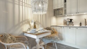 A modern kitchen with white cabinetry, a built-in oven, and a coffee machine. There is a dining table with chairs and a chandelier. - Lütt'n Witthüs - Whg. 6 (Wenningstedt-Braderup (Sylt))