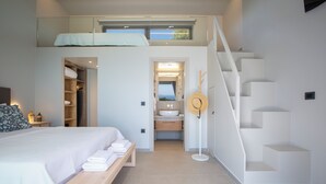 Un dormitorio moderno con una cama litera, una mesita de noche con toallas, un banco de madera y una escalera que lleva a un baño con vistas.