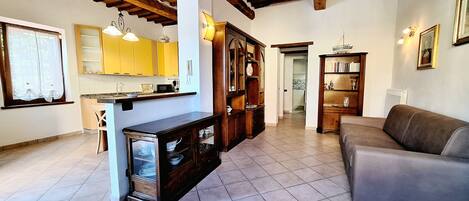 Amplia sala de estar con sofá, armarios de madera y cocina con muebles color amarillo y piso de baldosas.