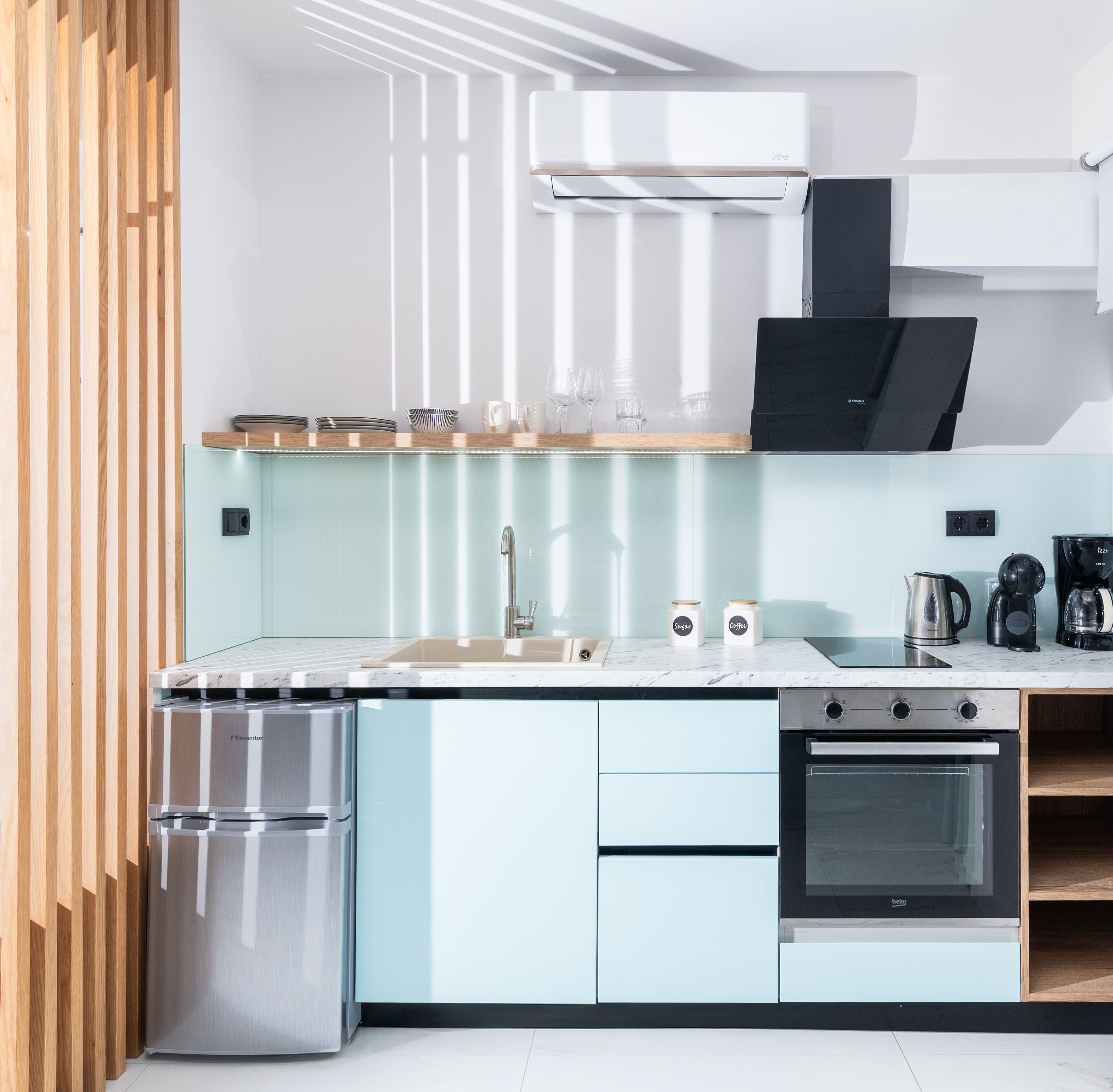 A modern kitchen with light blue cabinets, stainless steel appliances, and a wooden accent wall.