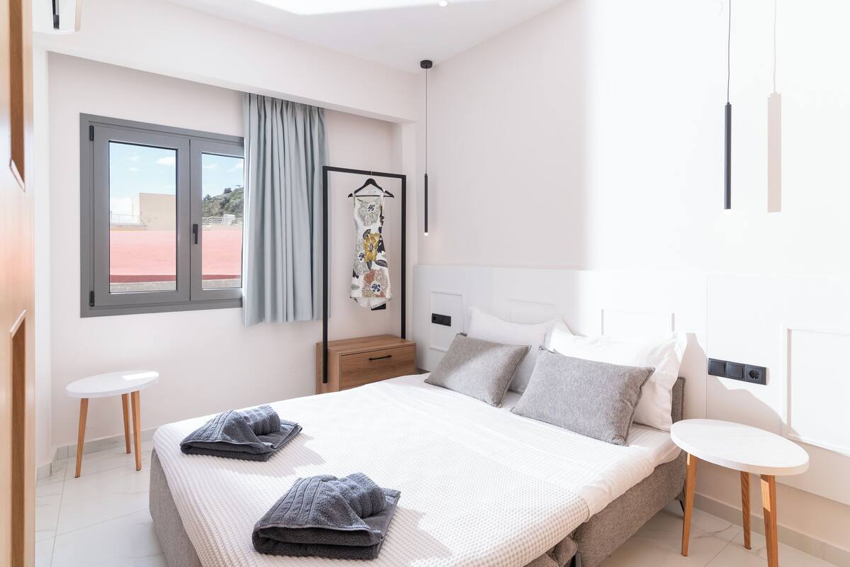 A modern hotel room with a large bed, bedside tables, a wardrobe, and a window with curtains.