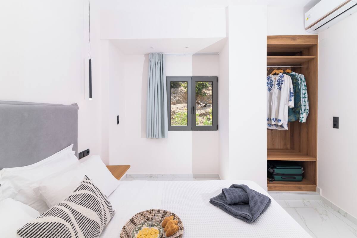 A modern bedroom with a bed, a window with curtains, a wooden wardrobe, and a small window view.