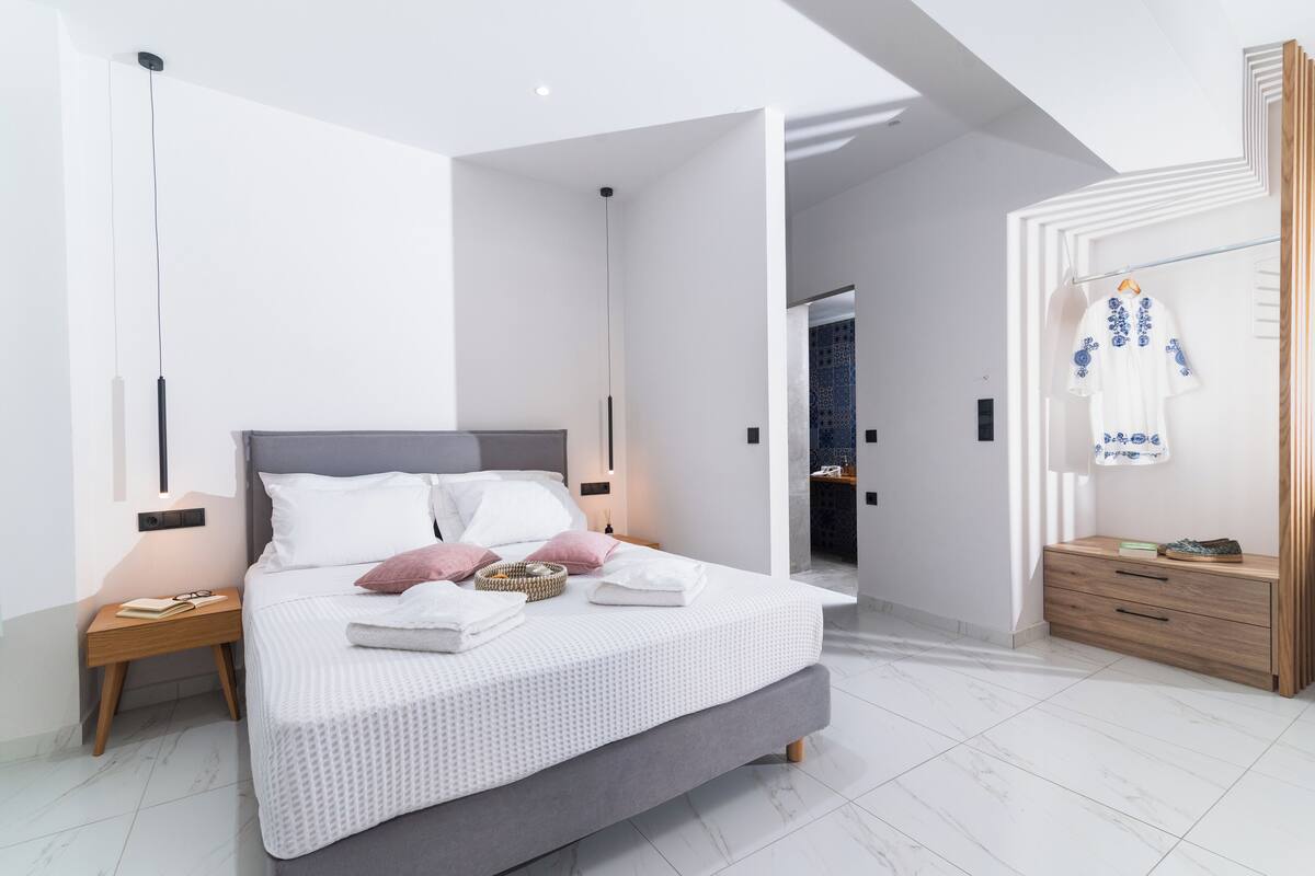A modern bedroom with a large bed, bedside tables, a wardrobe, and a bathroom visible through an open door.