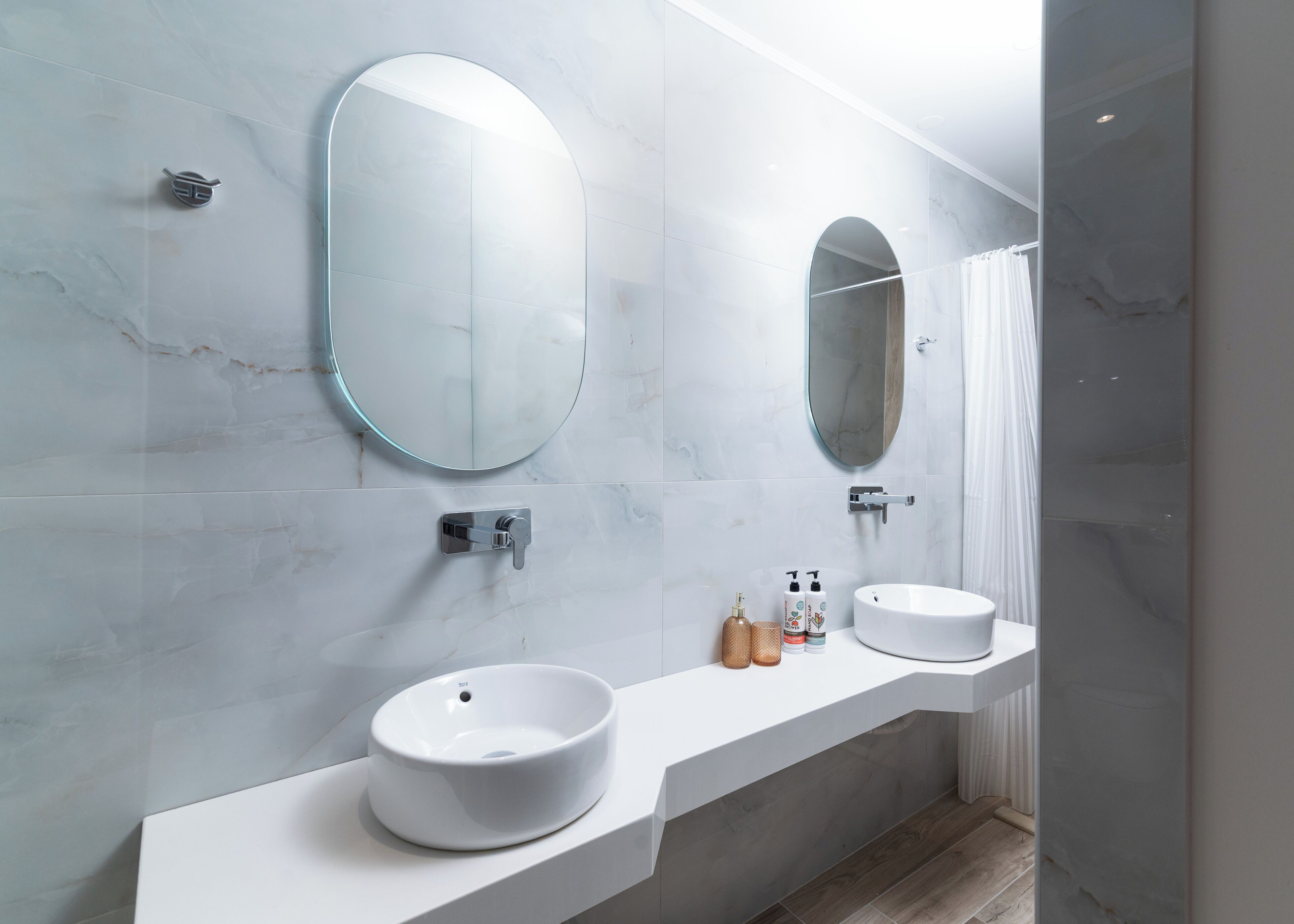 Un baño moderno con dos espejos redondos, un lavabo blanco y una zona de ducha.