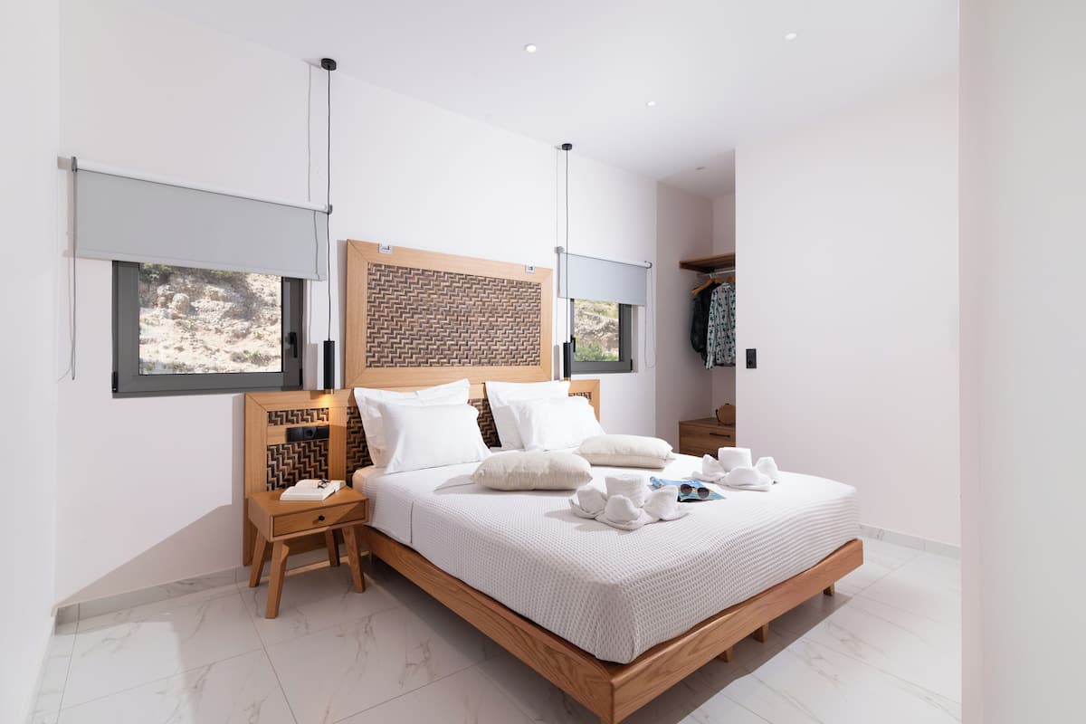 A modern bedroom with a large bed, wooden headboard, and a view of the outdoors through a window.