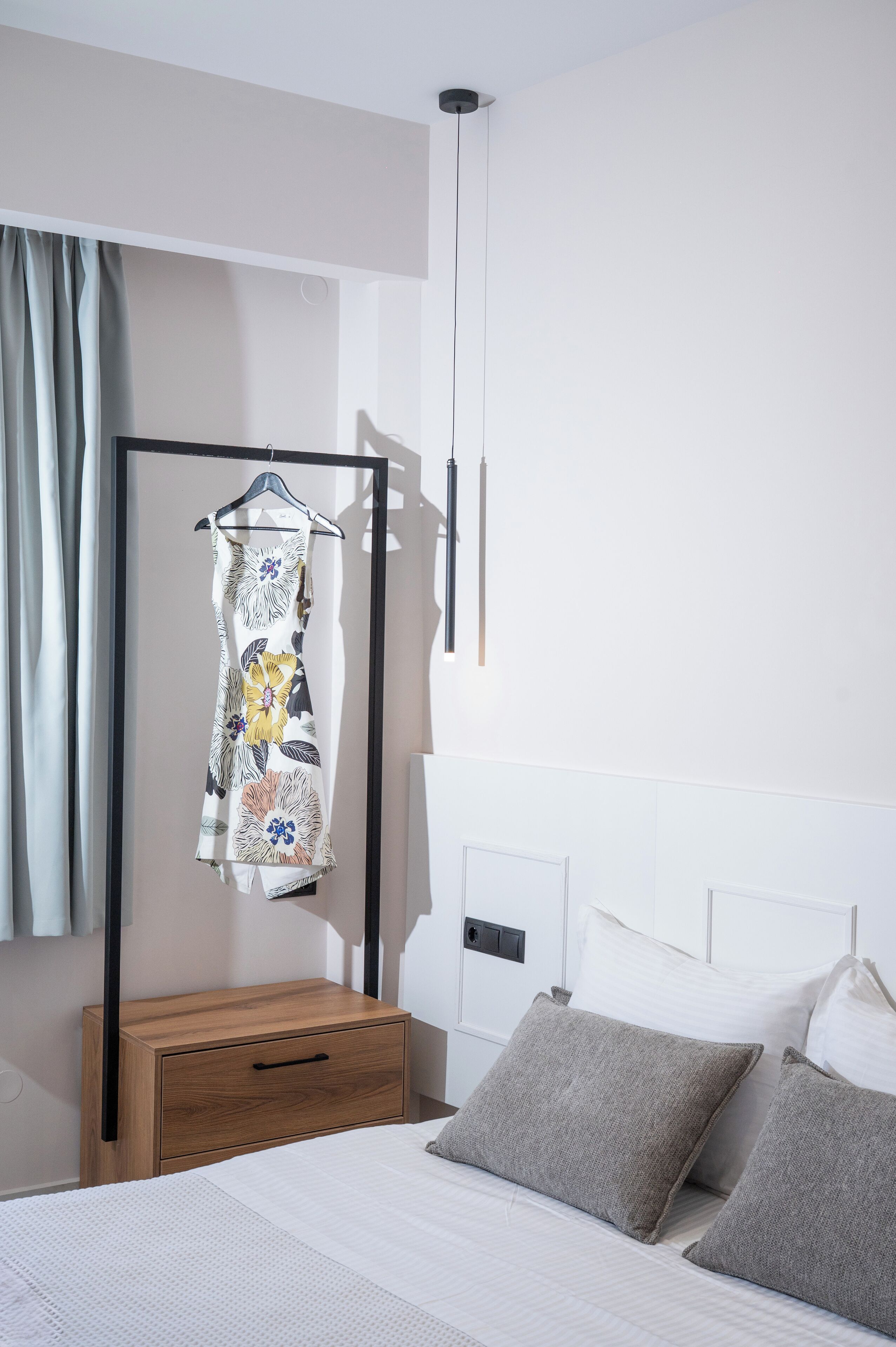 Quarto com cama, mesa de cabeceira de madeira, um cabideiro e cabeceira branca.