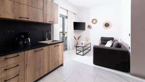 Une cuisine moderne avec des meubles en bois et un plan de travail noir, un canapé noir dans l’espace salon et un téléviseur à écran plat fixé au mur.