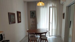 A dining area with a round table and chairs, a hanging light fixture, and a kitchen area with a microwave and oven.