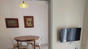A room with a round wooden dining table, four chairs, a wall-mounted TV, and two framed pictures.