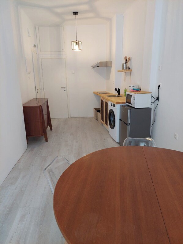 Cocina compacta con lavadora, microondas y una mesa de madera.