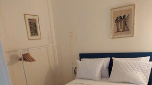 A neatly made bed with white linens and pillows, a wooden hanger rack, and two framed pictures on the wall.