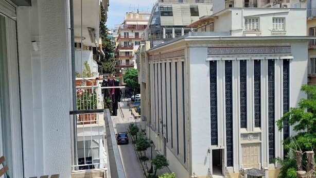 A narrow urban street with buildings on both sides, a clear sky, and a few pedestrians.
