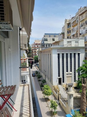 Una calle urbana estrecha flanqueada por edificios, cielo despejado y algunos peatones.