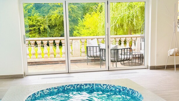 Un bain à remous avec un bord carrelé, un balcon avec des chaises et une vue sur la verdure.