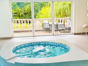 A hot tub with a tiled edge, a balcony with chairs, and a view of greenery.