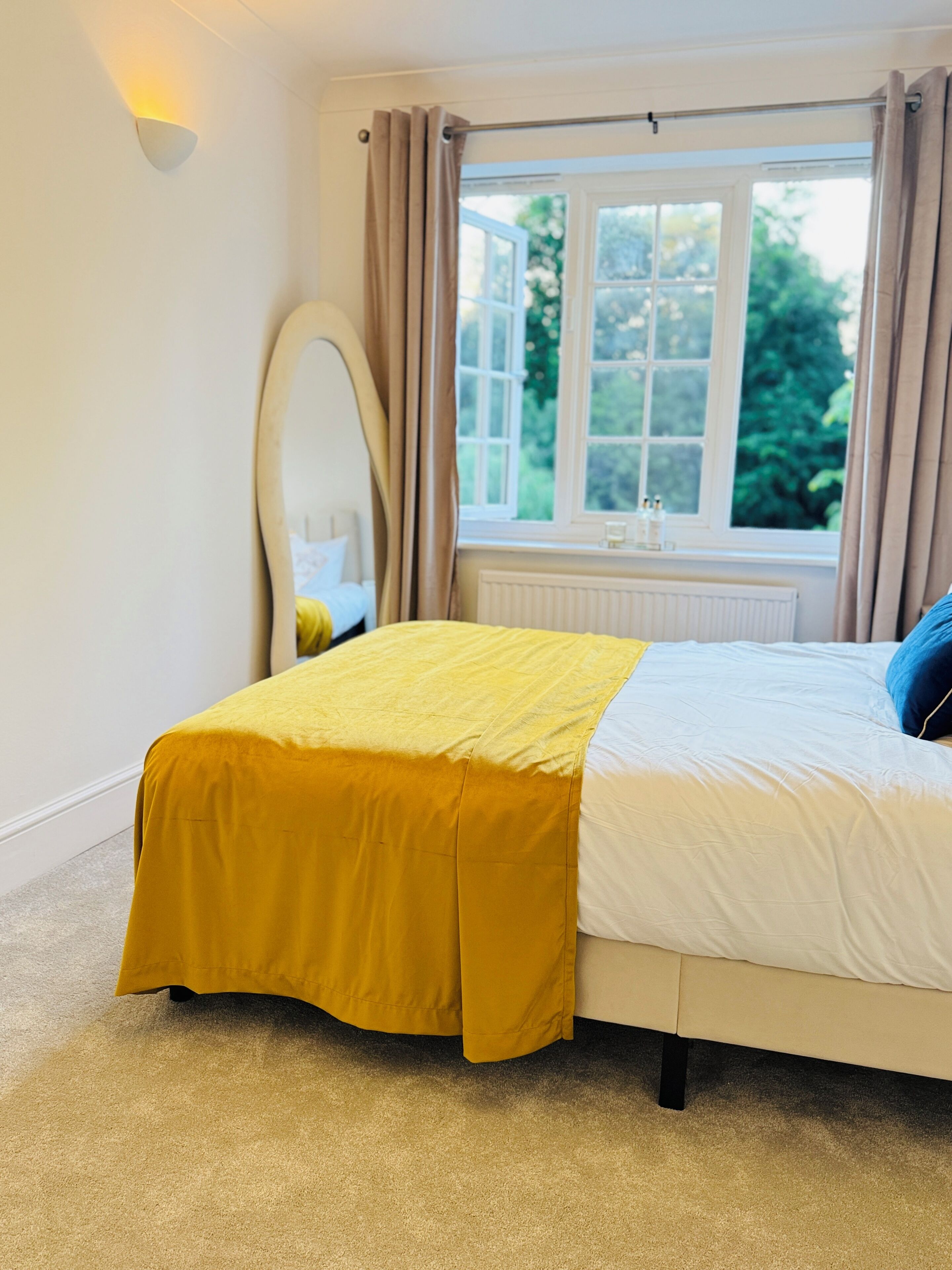 A bedroom with a bed, a window with curtains, a radiator, and a wall-mounted light fixture.
