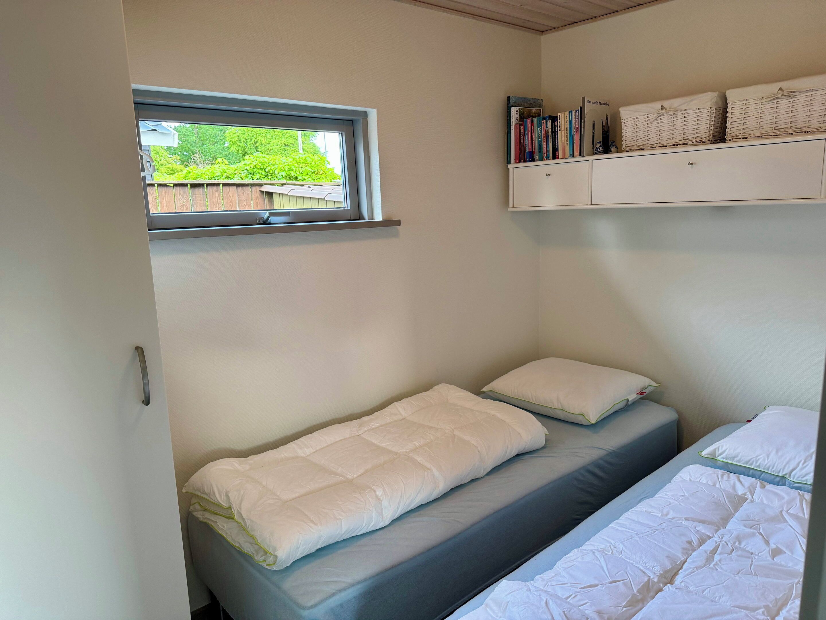 Una piccola camera con un letto singolo, una finestra, una mensola con libri e un armadio bianco.
