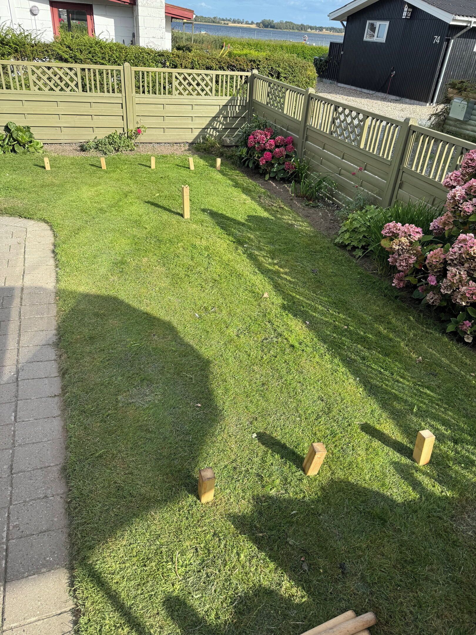 A well-maintained lawn with wooden posts, a wooden fence, and a house in the background.