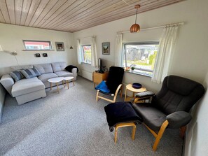 A furnished living room with a sofa, armchairs, a small table, and a television.