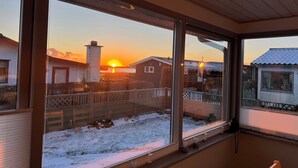 A room with large windows, a wooden ceiling, and a view of a sunset over a snow-covered landscape.