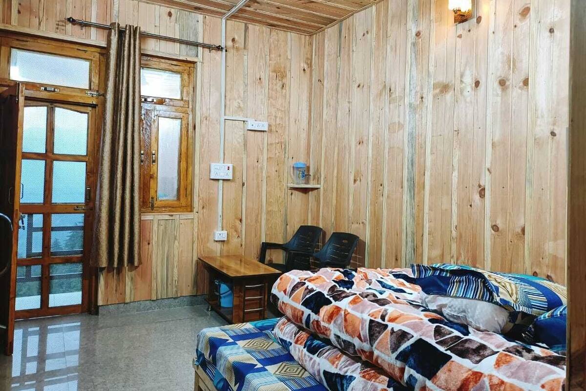 A wooden cabin interior with a bed, a table, chairs, and a ceiling fan.