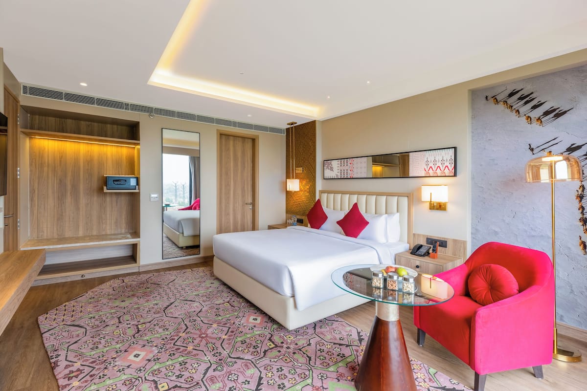 Een moderne hotelkamer met een groot bed, een rode fauteuil, een glazen salontafel en een televisie aan de muur.
