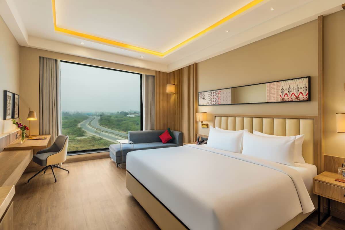 Een hotelkamer met een groot bed, een bureau, een stoel, een bank en een groot raam met uitzicht.