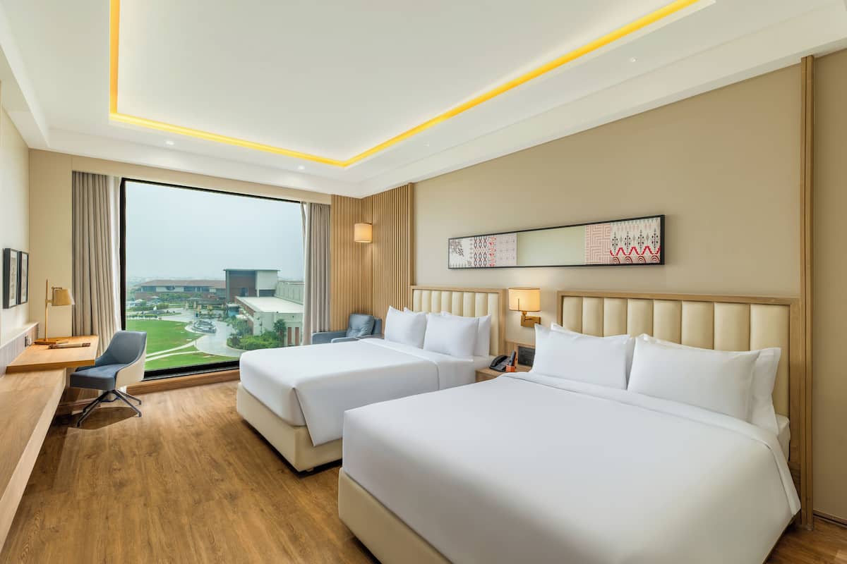 Een hotelkamer met twee bedden, een bureau, een stoel, een groot raam met uitzicht en een plafond met inbouwverlichting.