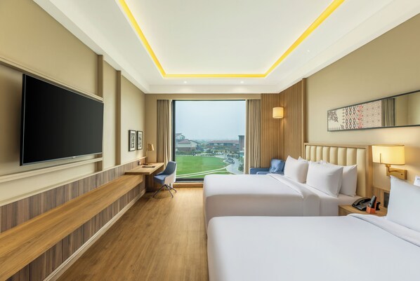 A hotel room with a large TV, two beds, a desk, and a view of a cityscape. - The Aaureum Resort & International Convention Centre (Bhilwara)
