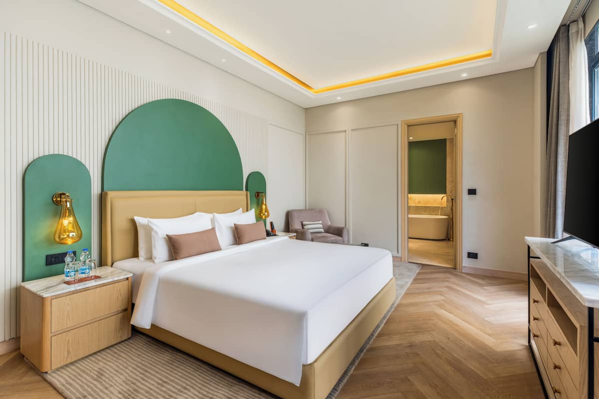 Een moderne hotelkamer met een groot bed, nachtkastjes, een televisie en een badkamer die door een open deur zichtbaar is.