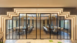 A modern dining area with a long table, multiple chairs, and a glass partition. - The Aaureum Resort & International Convention Centre (Bhilwara)