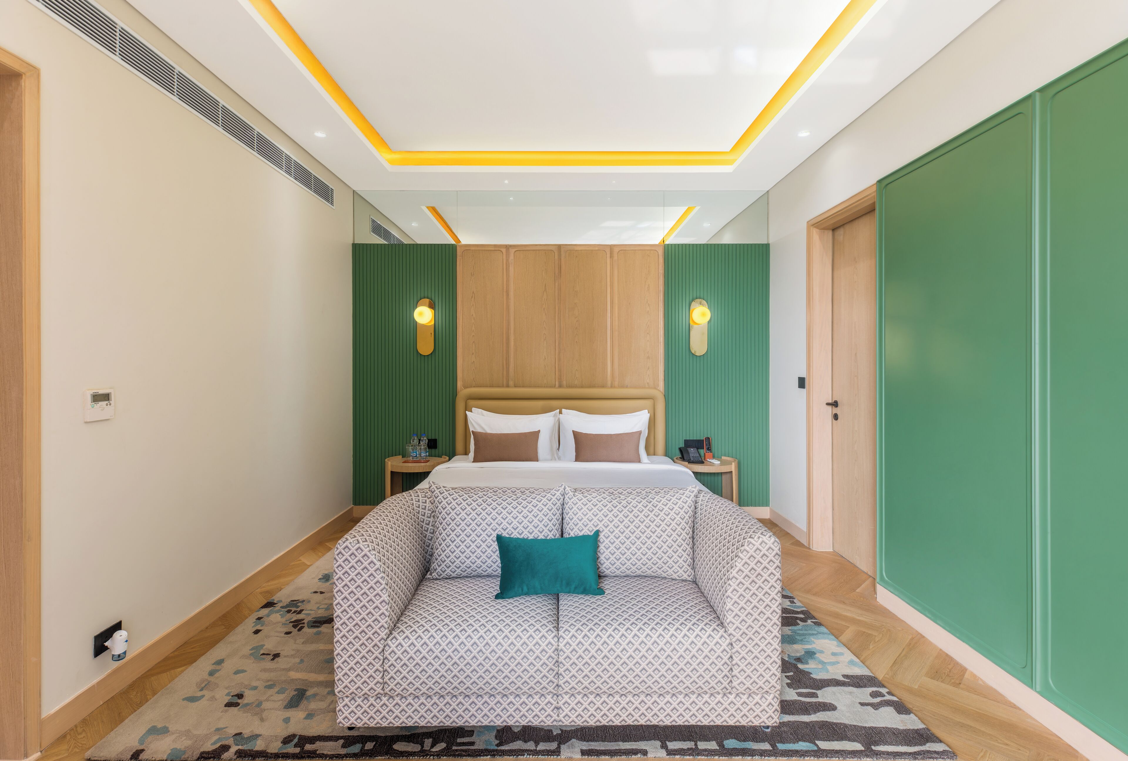 A bedroom with a bed, a sofa, a green wall, and a wooden door.