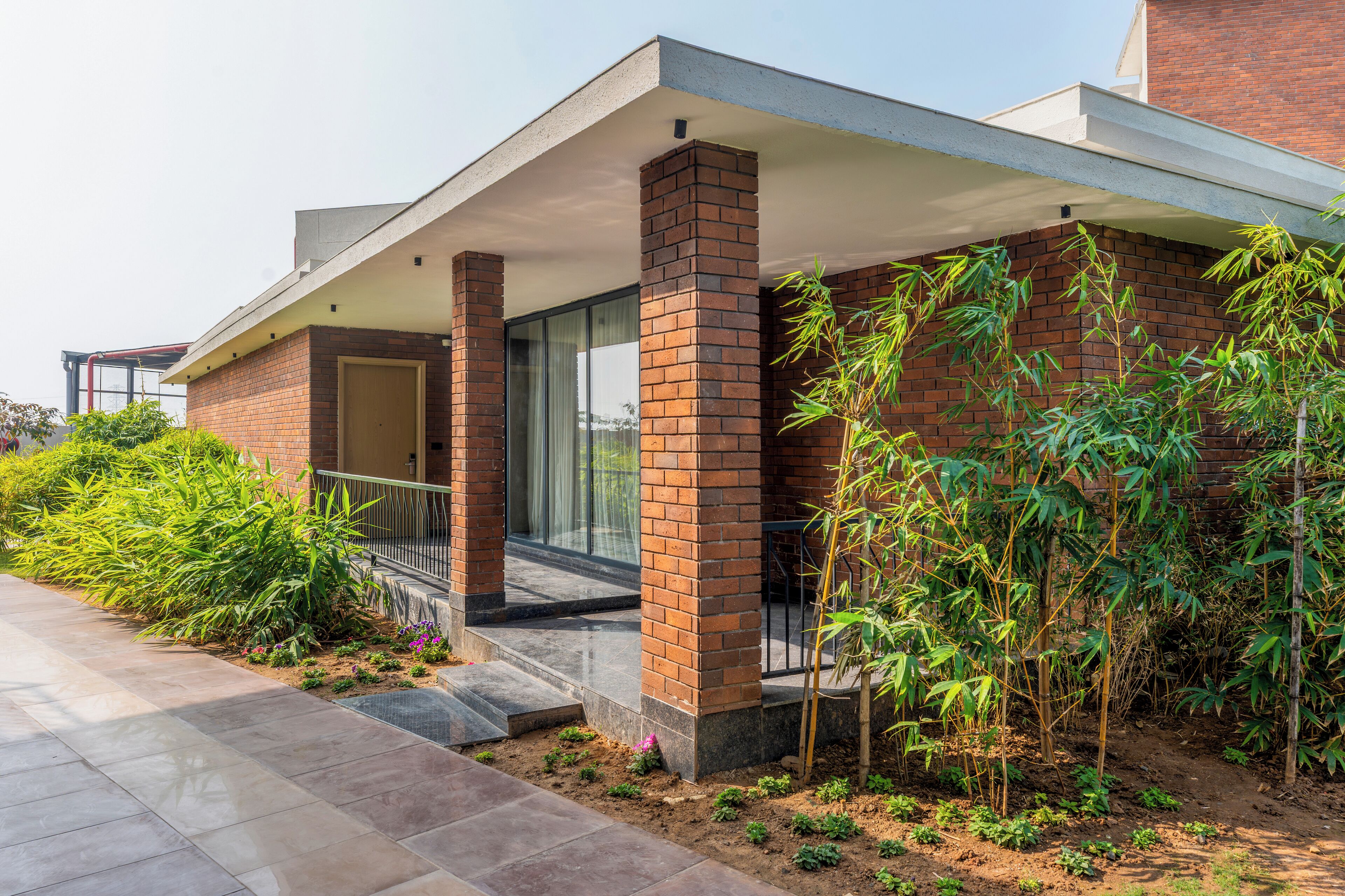 A modern house with a brick exterior, a covered porch, and a garden with various plants.