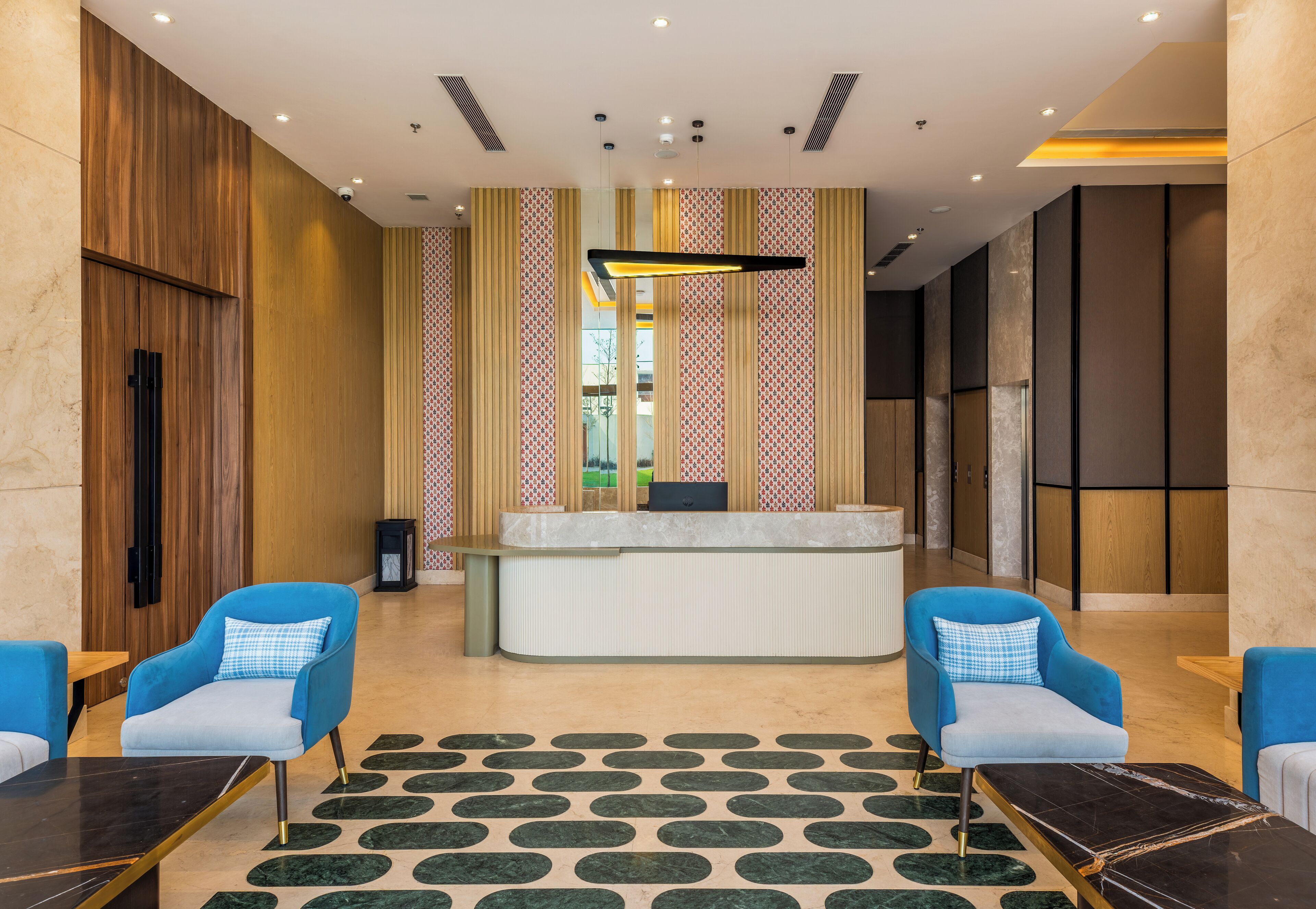 A reception area with a marble floor, two blue armchairs, a reception desk, and patterned curtains.