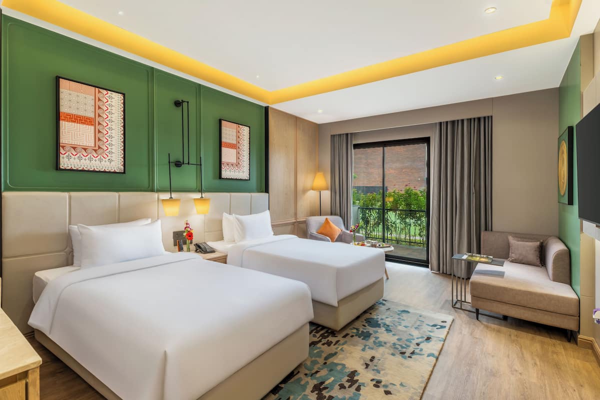 Een hotelkamer met twee bedden, een bank, een kleine tafel en uitzicht op groen.