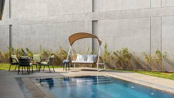 Una piscina con una sedia a dondolo, due poltrone da relax e un tavolino.