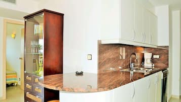 Een moderne keuken met een marmeren aanrecht, witte kastjes en een ingebouwde wijnrek.