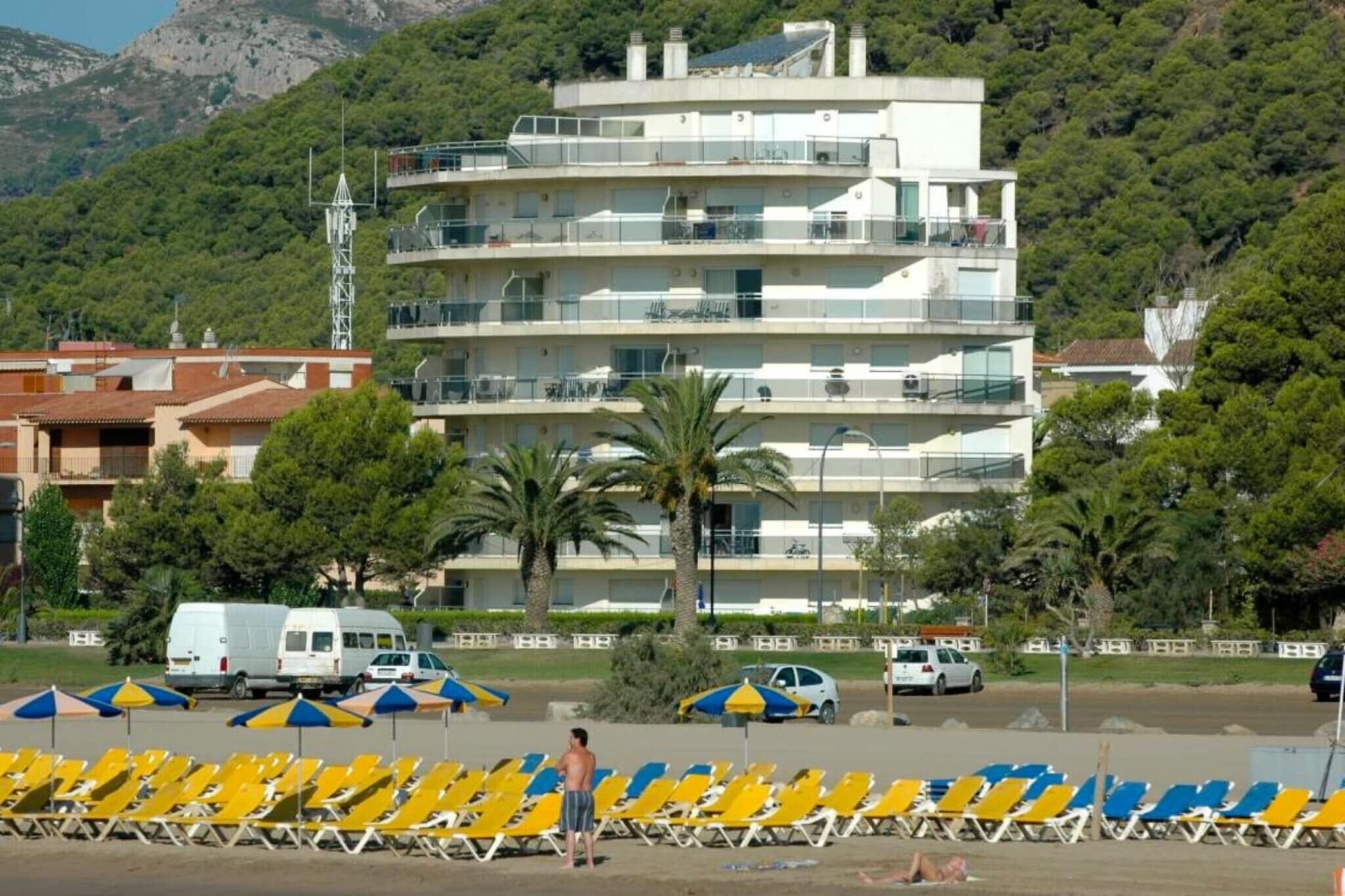 Un edificio de varios pisos con balcones, un estacionamiento con coches y sillas de playa.