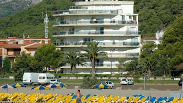 Un edificio de varios pisos con balcones, un estacionamiento con coches y sillas de playa.