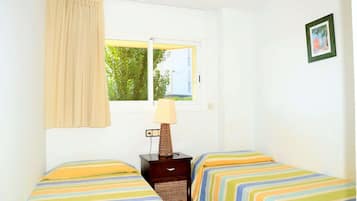 Una habitación con dos camas, una ventana con vistas a la vegetación, una lámpara en una mesita de noche y un cuadro en la pared.