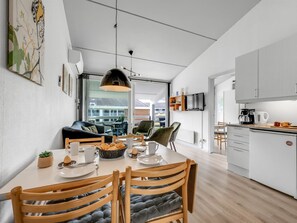 A modern kitchen with a dining area, a TV mounted above the counter, and a view of the outside.