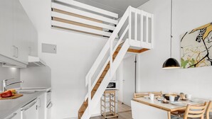 Eine moderne Küche mit weißen Schränken, einer Holztreppe und einem Essbereich mit weißem Tisch und Stühlen.