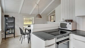 Eine moderne Küche mit weißen Schränken, einer eingebauten Mikrowelle und einem Essbereich mit Tisch und Stühlen.