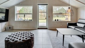 Ein geräumiges Loft mit hohen Decken, großen Fenstern, einem Ledersofa, einem gepolsterten Ottomanen und einer Pendelleuchte.