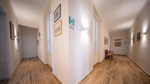 A hallway with wooden flooring, framed pictures on the walls, and a sign indicating an emergency exit. - Mantellate 9 (Florence)