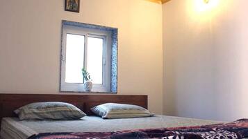 Une chambre à coucher avec un lit, deux oreillers, une fenêtre avec une plante et un luminaire fixé au mur.